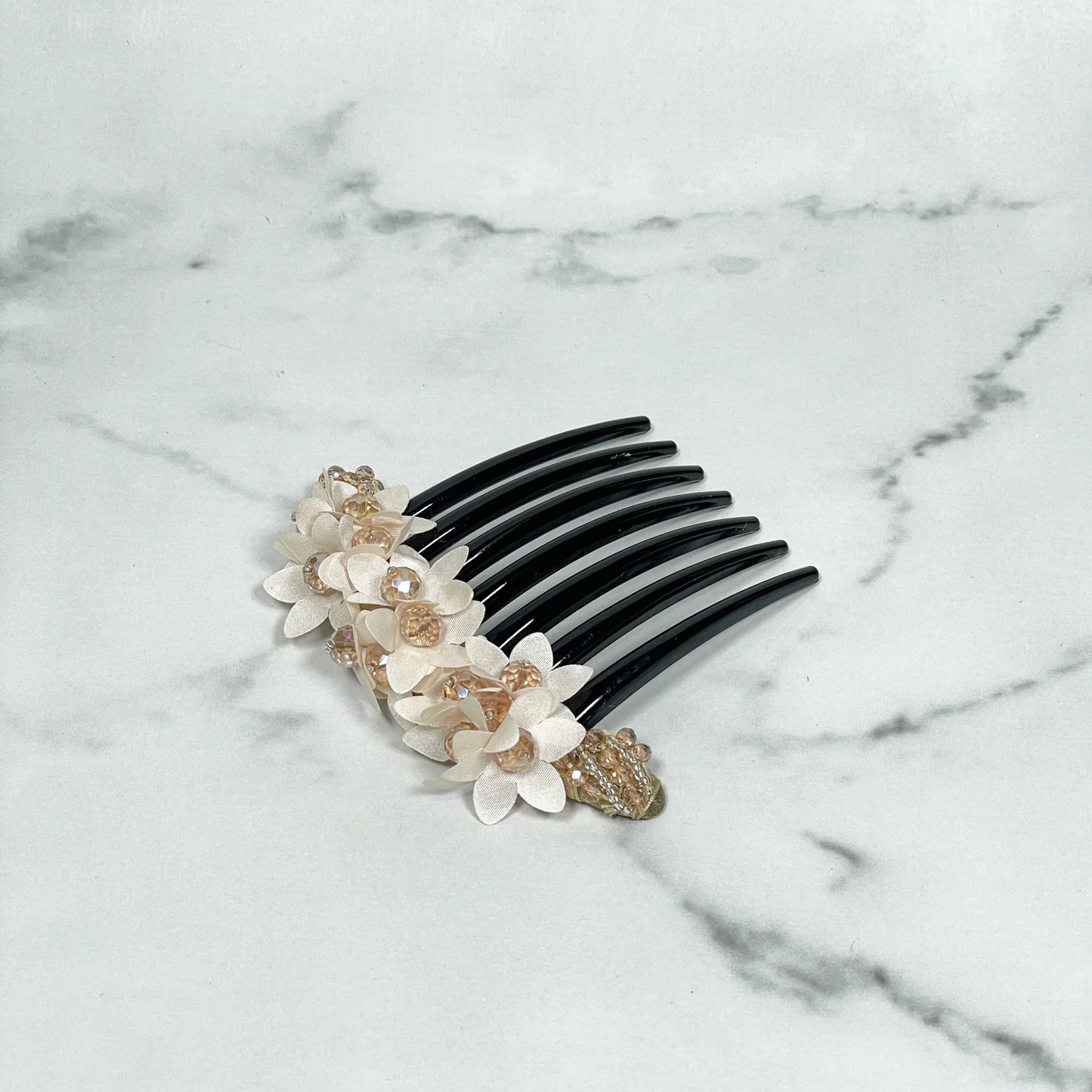 Black studded hair bun comb adorned with white and gold floral decorations on marble surface