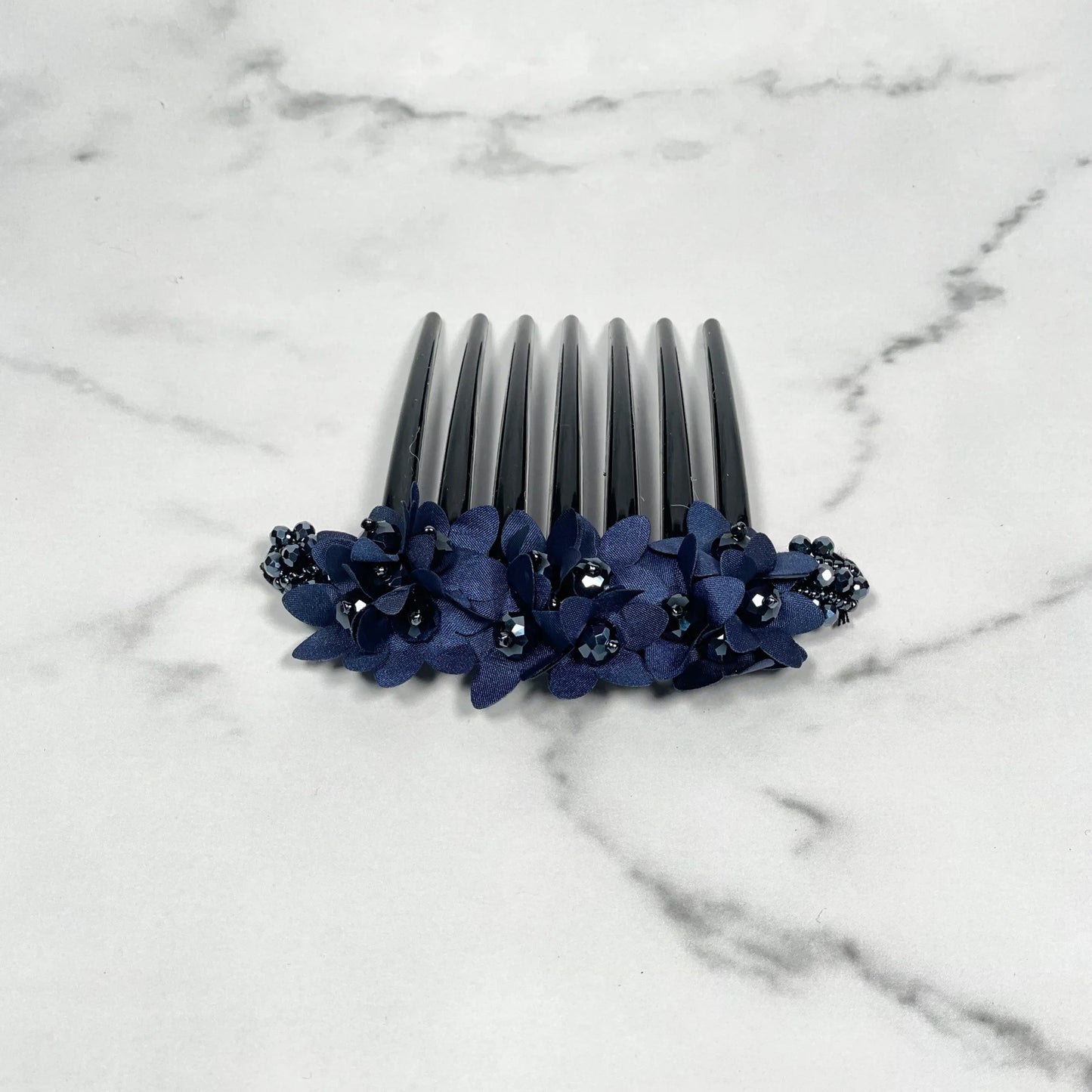 Black studded hair bun comb adorned with dark blue flower decorations on a marble surface