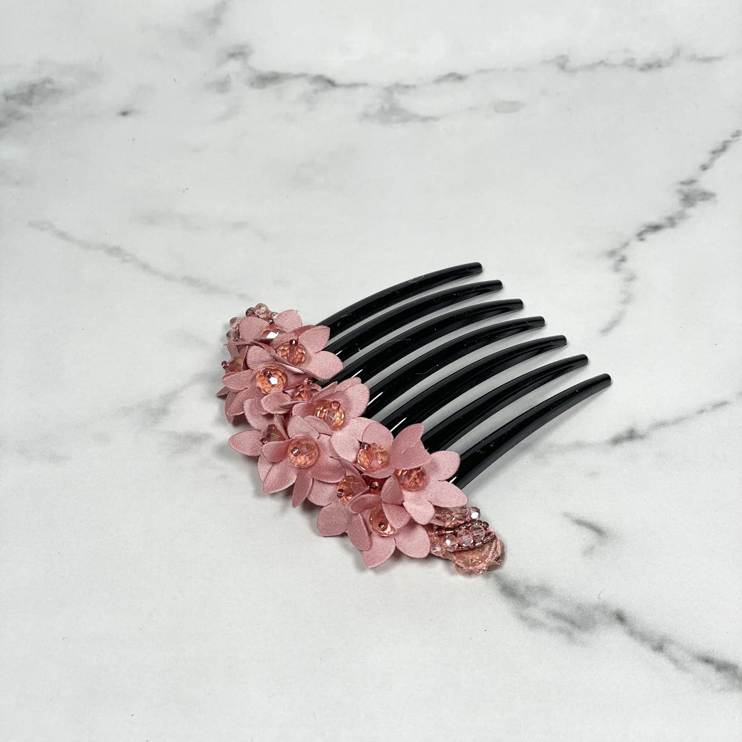 Black studded hair bun comb with pink floral decoration and rhinestone accents on marble background