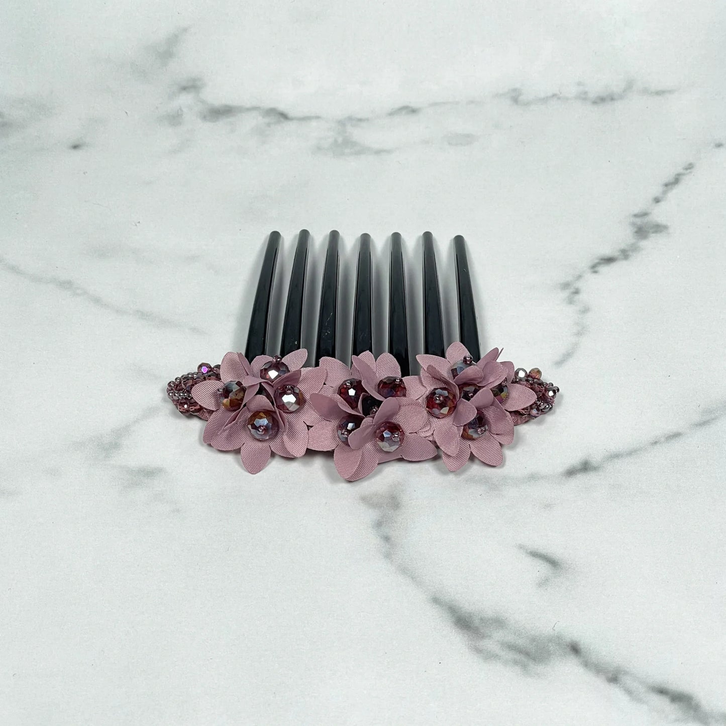Black studded hair bun comb decorated with pink flowers and rhinestones on marble surface