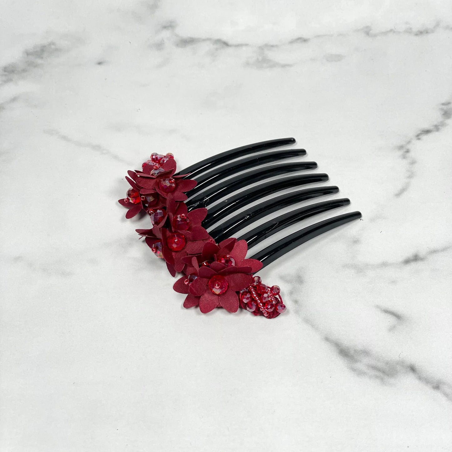 Black studded hair bun comb with red floral decorations on a white marble surface
