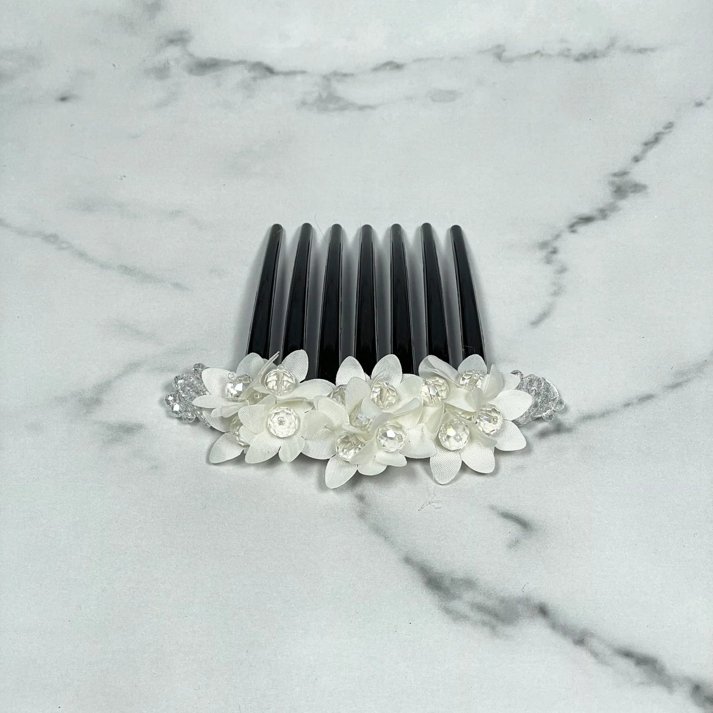 Studded hair bun comb with white floral decorations and clear rhinestones on black plastic comb