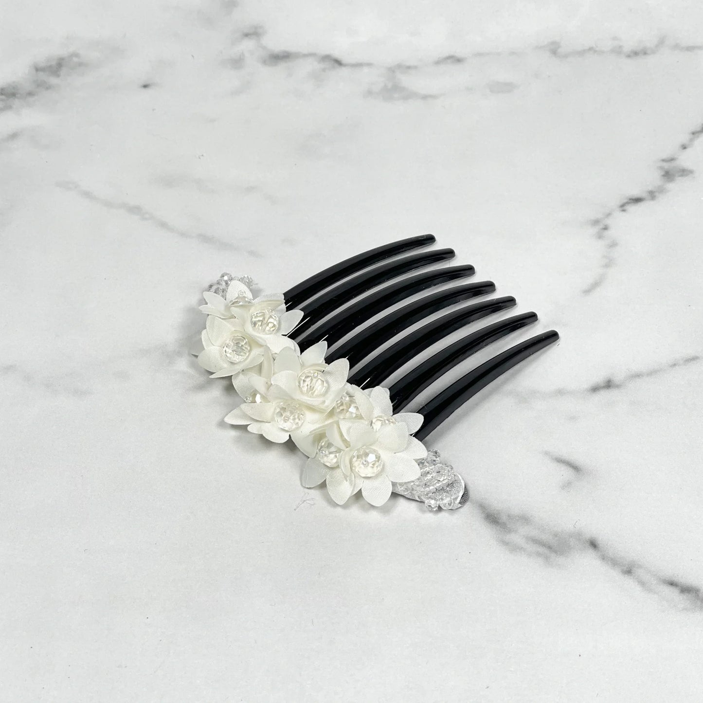 Black studded hair bun comb with white floral decorations and clear crystal accents on marble surface