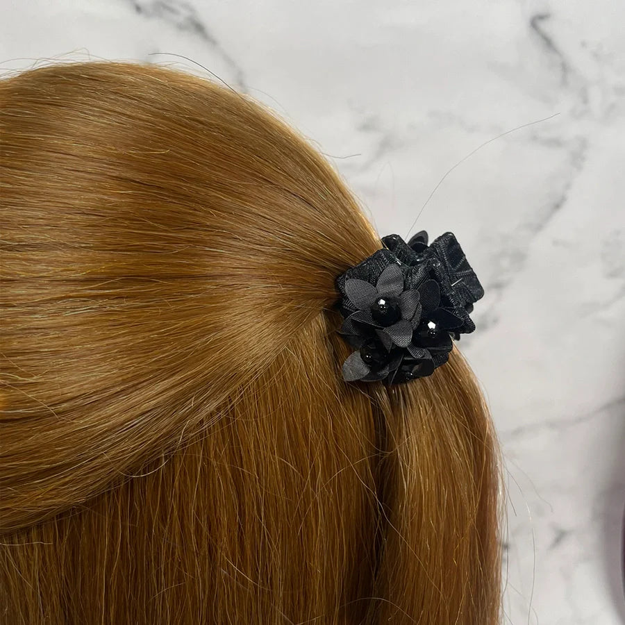 Black floral studded hair clutches securing light brown hair against a marble background