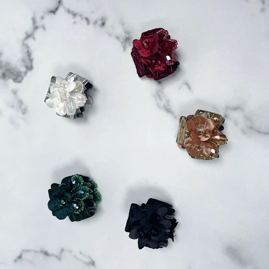 Set of five colorful studded hair clutches with flower designs on a white marble background