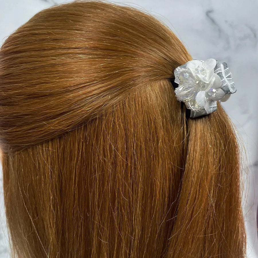 White floral studded hair clutches holding back light brown hair against a marble background