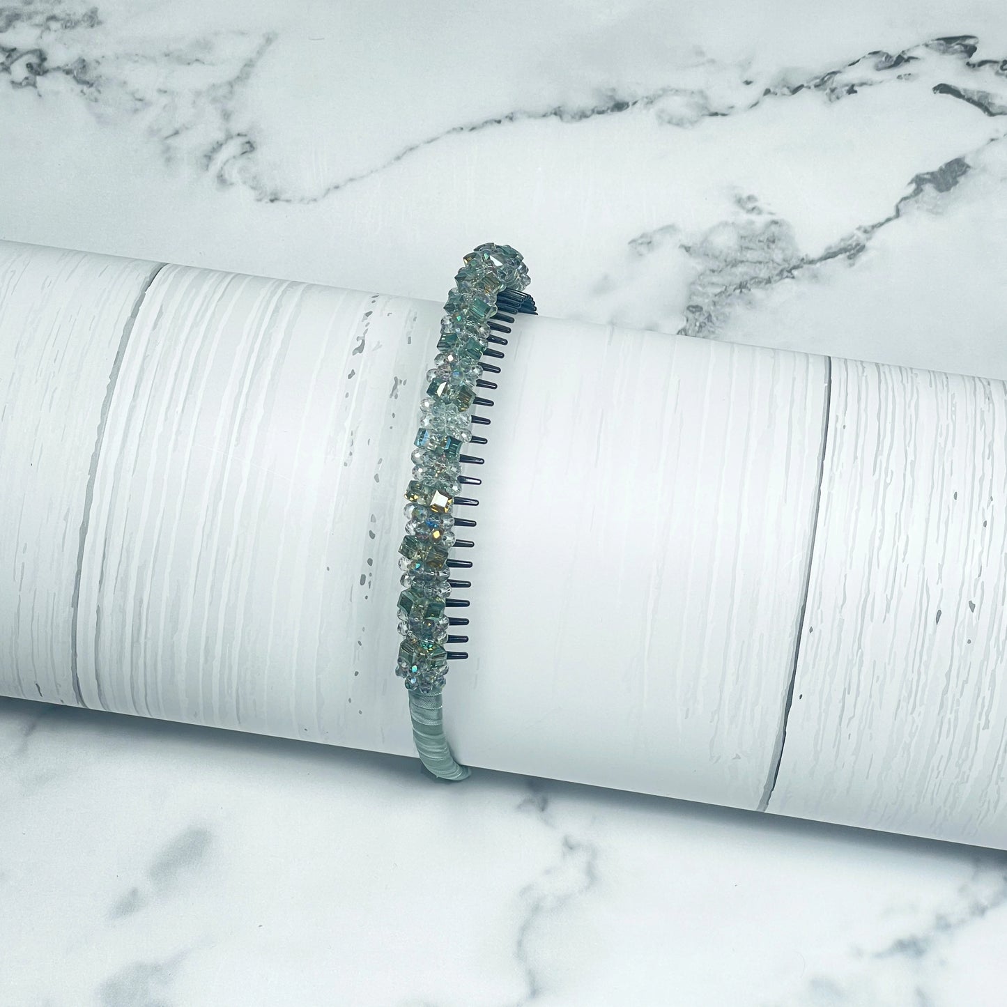Studded headbands with green and clear crystals on a white textured cylindrical display