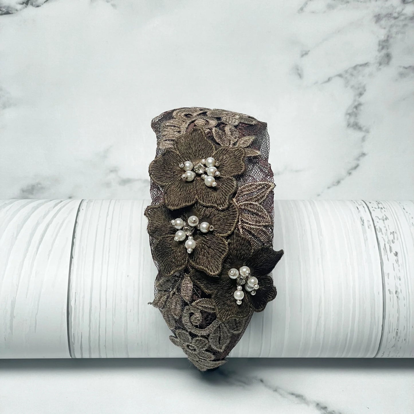 Three flower broad hairbands featuring brown lace and pearl embellishments on a white wooden background