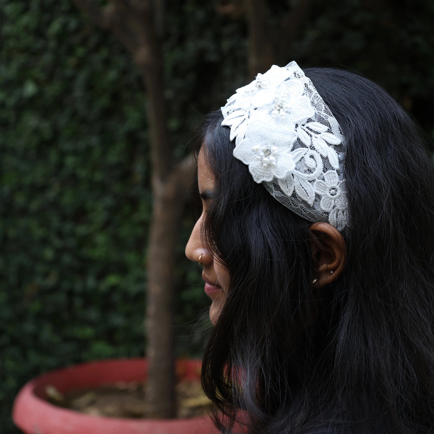 Woman wearing a white lace three flower broad hairbands outdoors with dark hair and green background