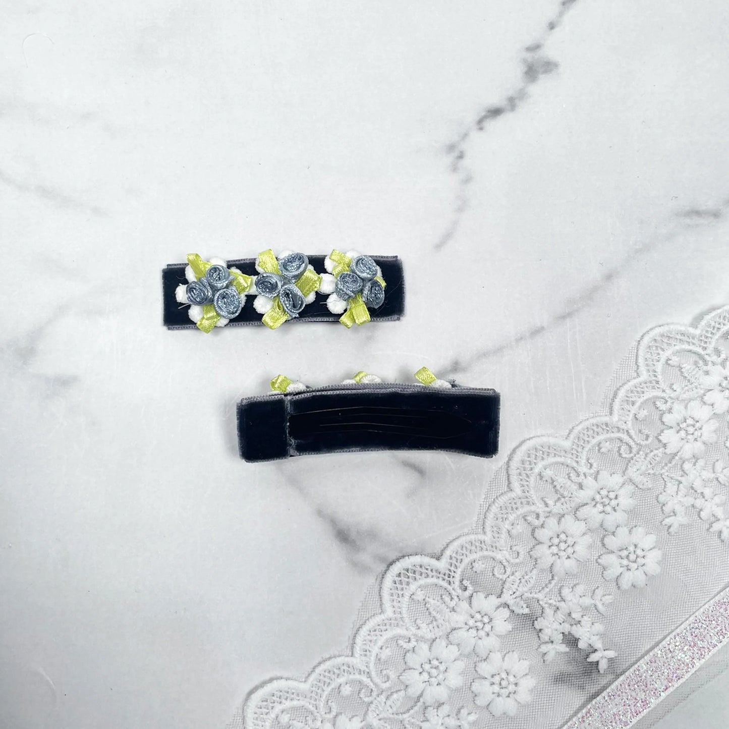 Black velvet flower hair pins with small gray and yellow fabric flowers on a marble surface