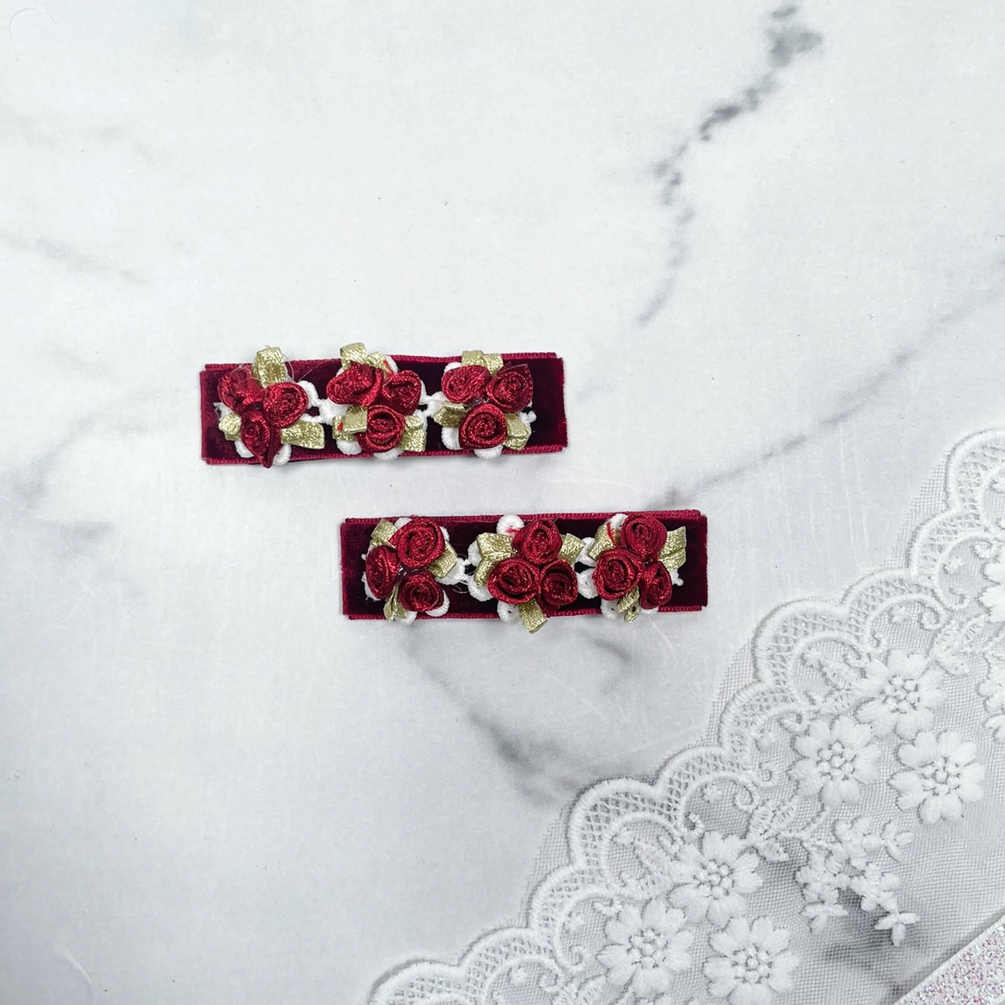 Pair of red velvet flower hair pins with embroidered roses and gold leaves on marble background
