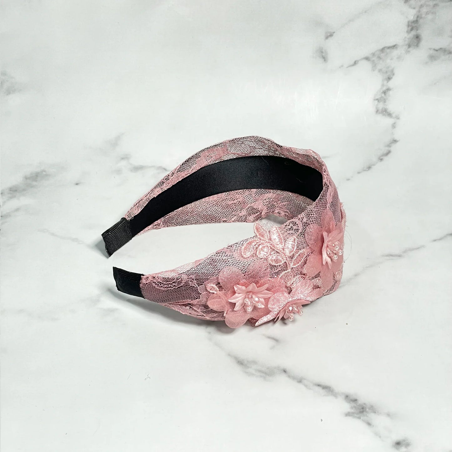Pink broad shimmery lacy hairbands with floral appliques and black inner lining on marble surface