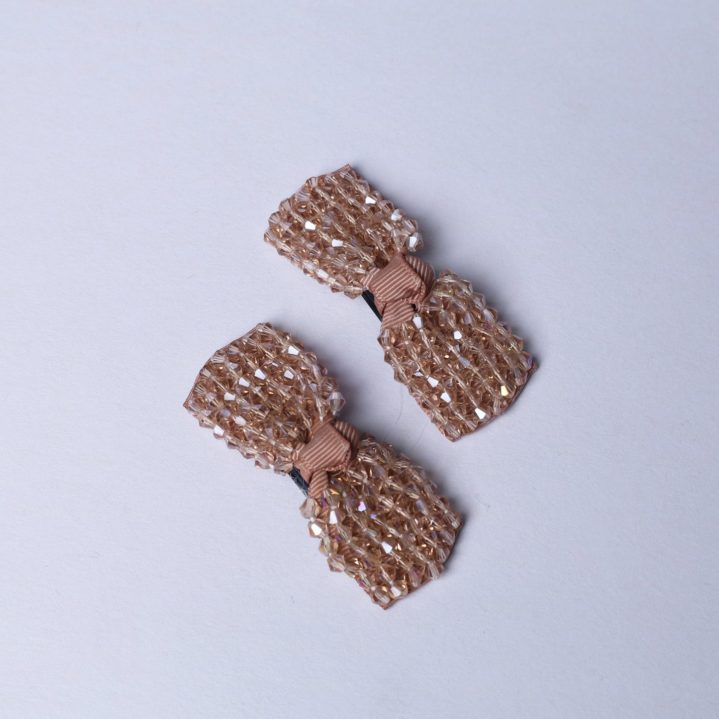 Pair of beige crystal bow hair pins with sparkling beads and fabric center on light background