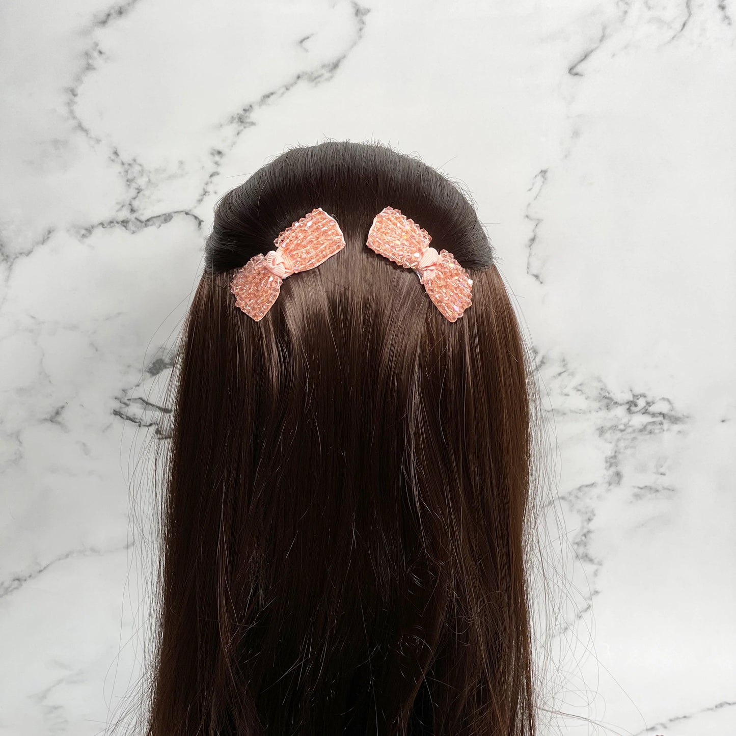Rose gold crystal bow hair pins clipped on dark brown straight hair against marble background