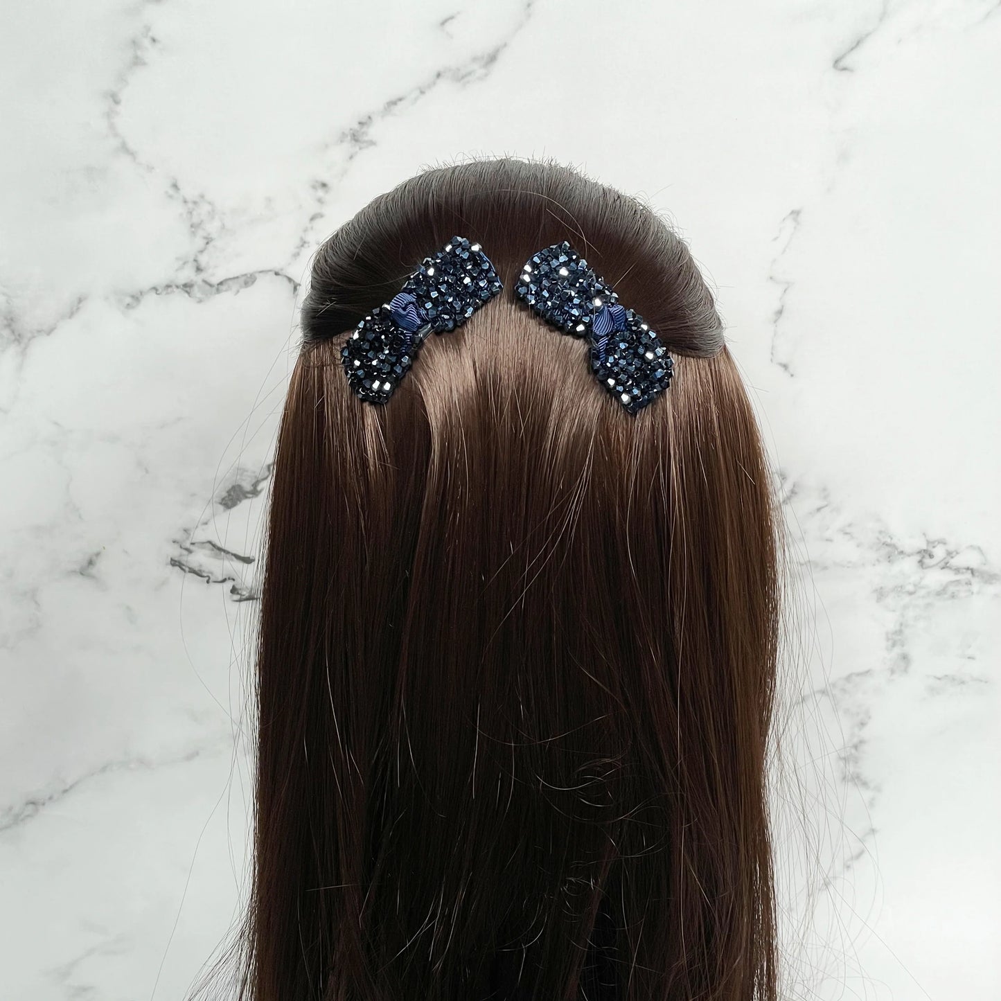 Black crystal bow hair pins attached to brown hair against a white marble background