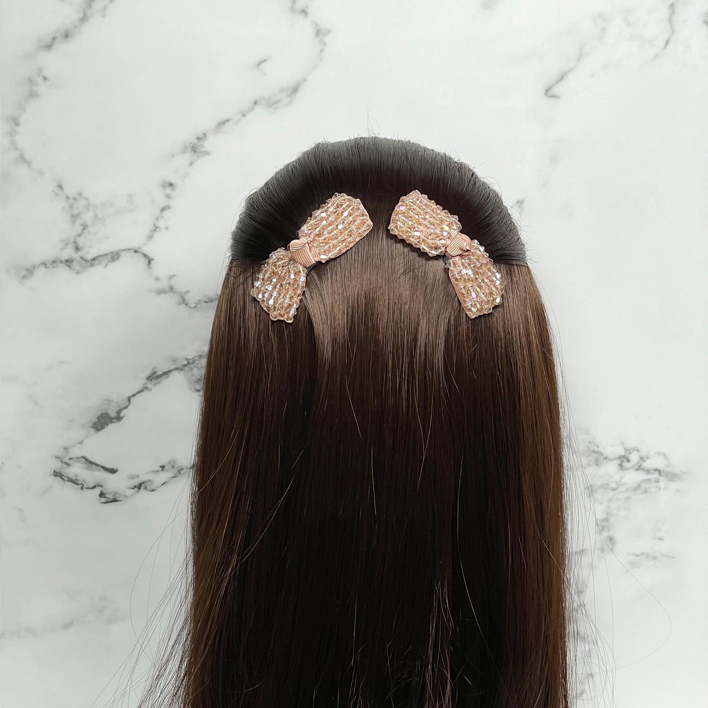 Crystal bow hair pins in light pink attached to dark brown hair on a marble background