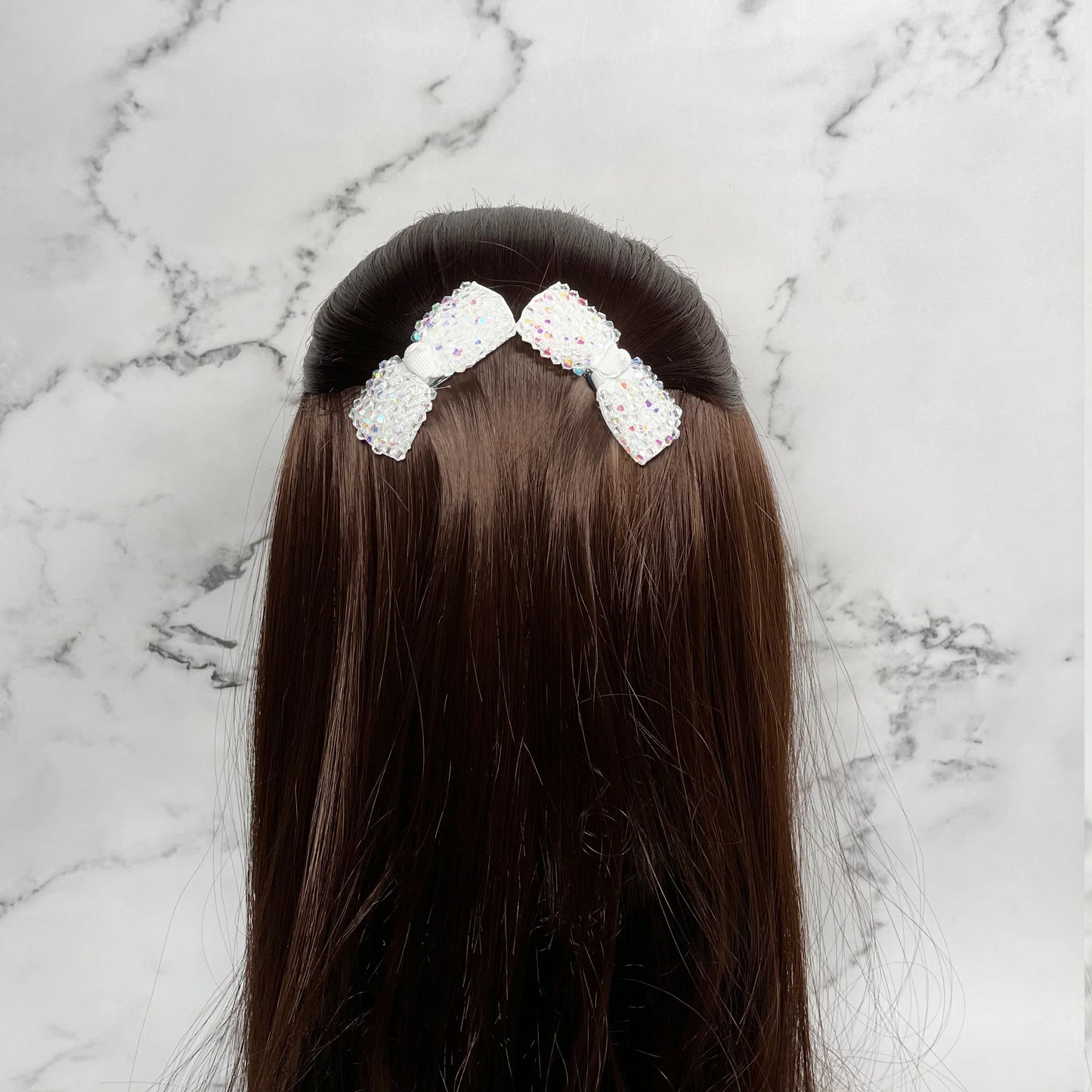 White crystal bow hair pins styled in long brown hair against a marble background