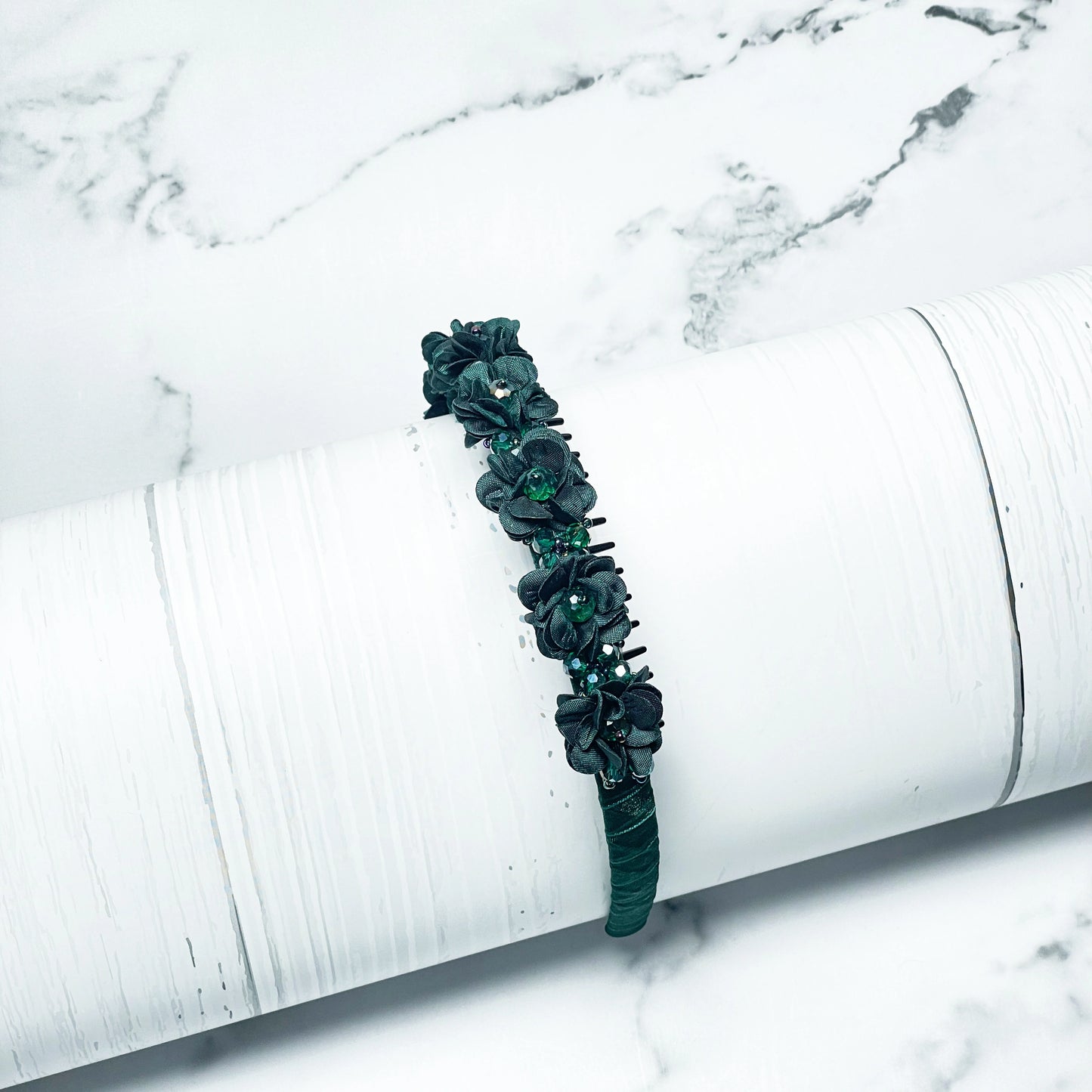 Dark green Crystal Studded Floral Hairbands with detailed flower designs on white marble background