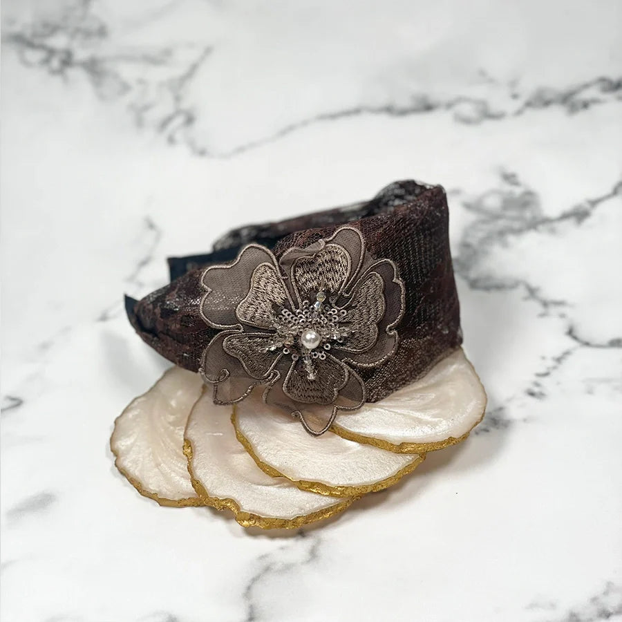Black lacy embellished hairbands for women with floral design and pearl detail on marble background