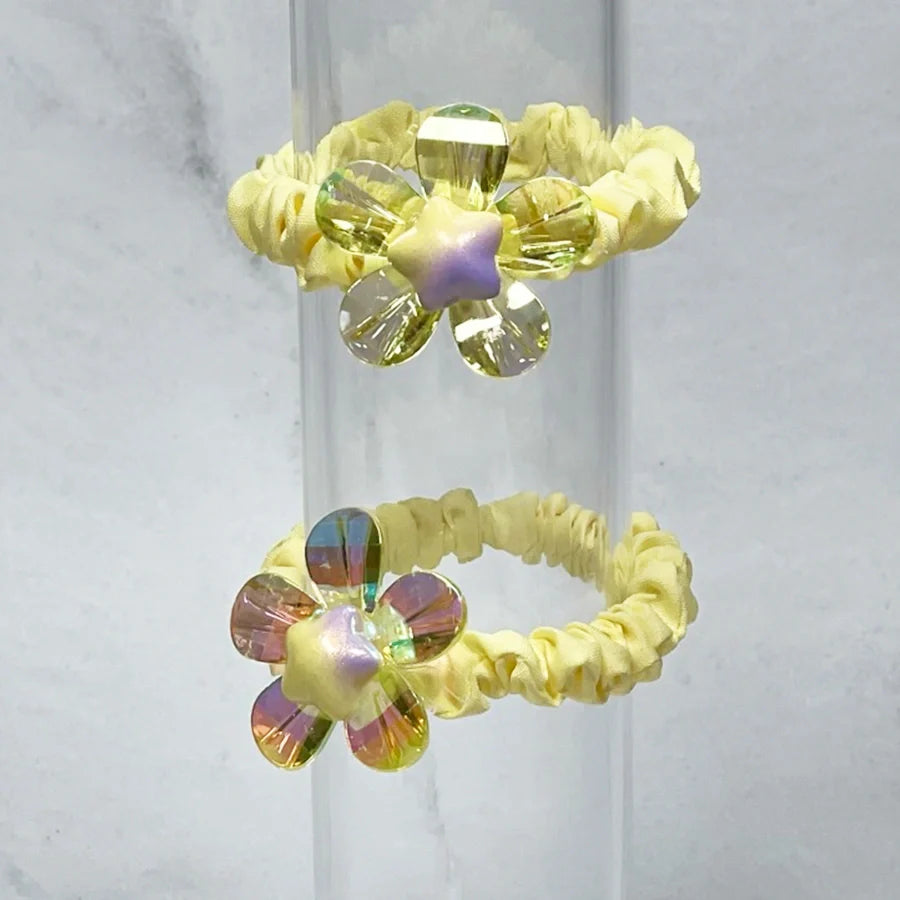 Yellow scrunchie hair ties featuring shiny daisy flower hair ties with iridescent petals and star centers
