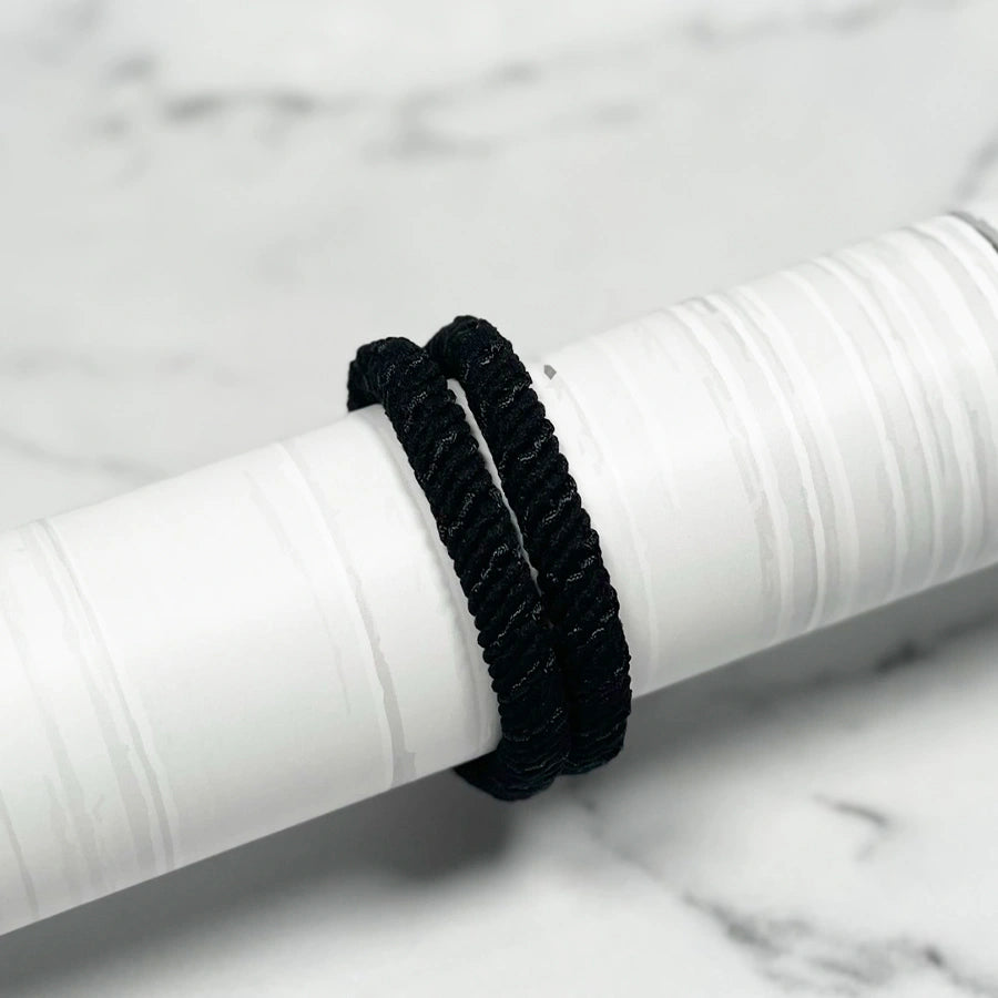 Black thick pastel hair ties shown on a white cylindrical holder on marble surface