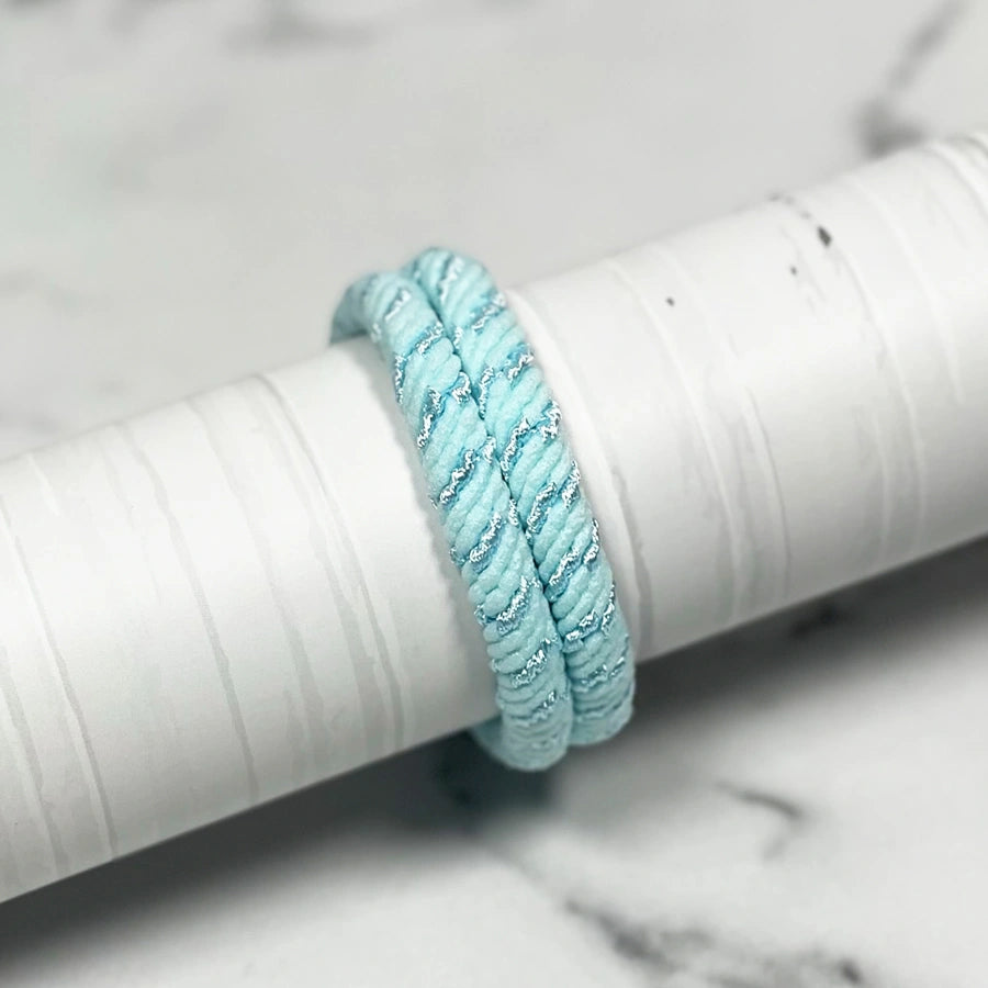 Light blue thick pastel hair ties with silver accents wrapped around a white cylindrical holder