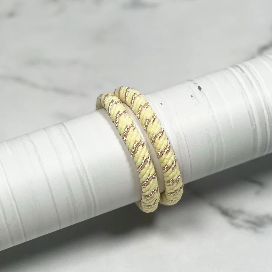 Pair of thick pastel hair ties in soft yellow with glitter accents wrapped around a white cylindrical object