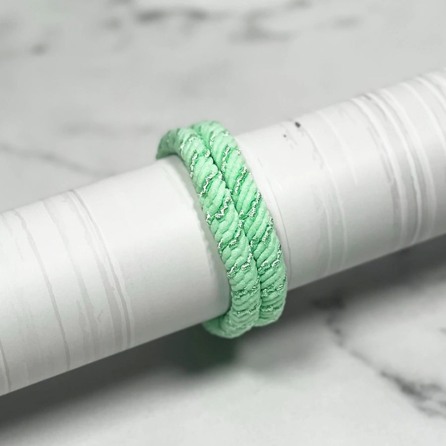 Thick pastel hair ties in light green twisted design displayed on white cylindrical holder