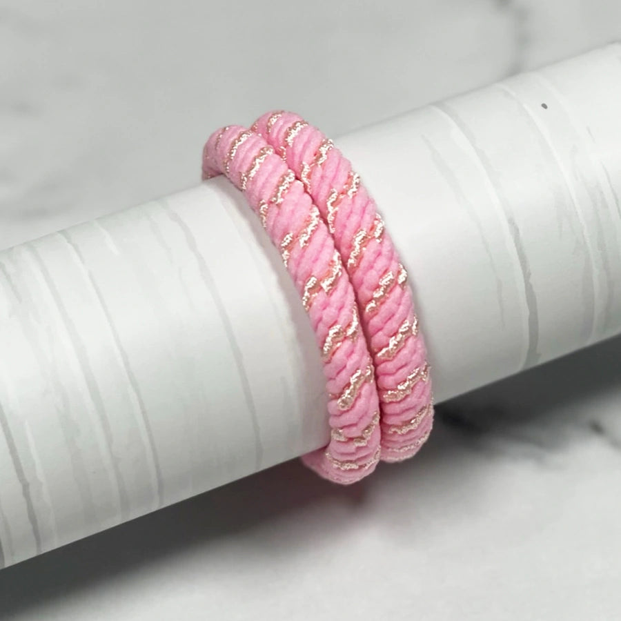 Two pink thick pastel hair ties with gold accents wrapped around a white cylindrical object