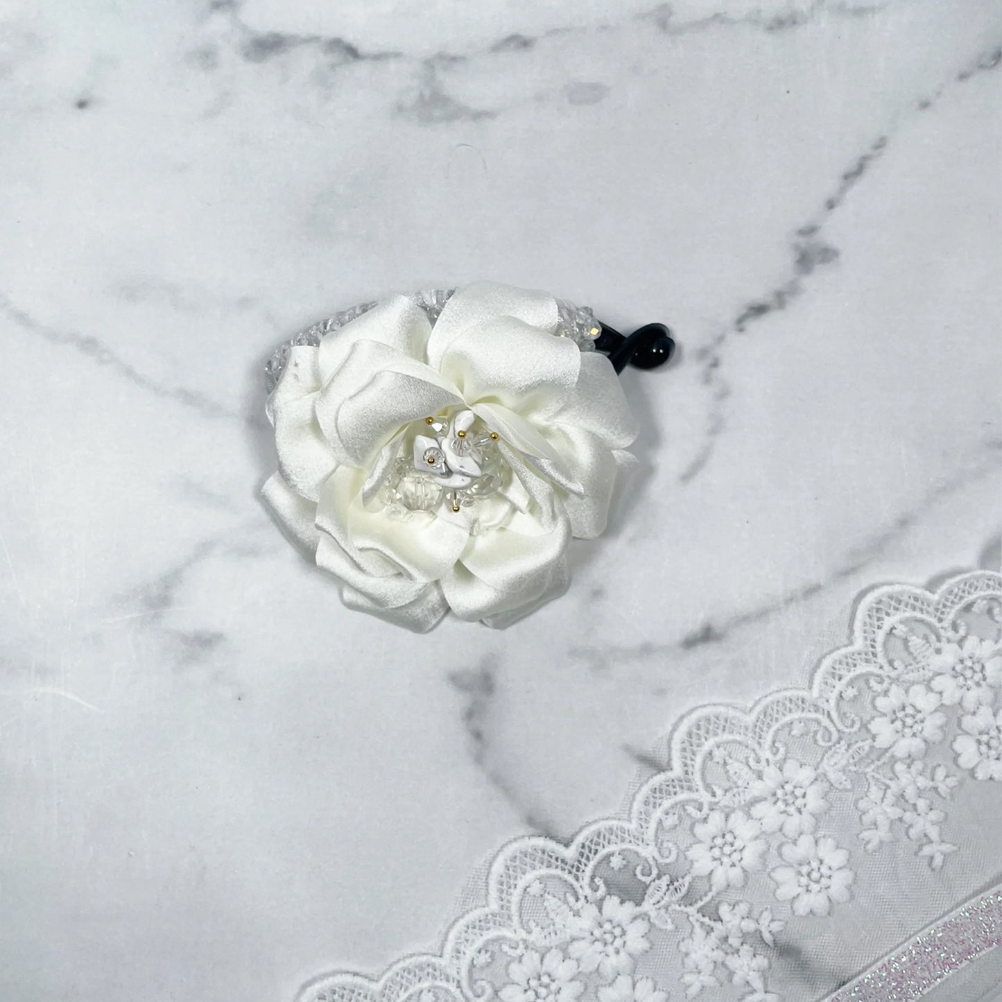 Bella Luxe white crystal banana clip with flower design on marble surface and lace fabric