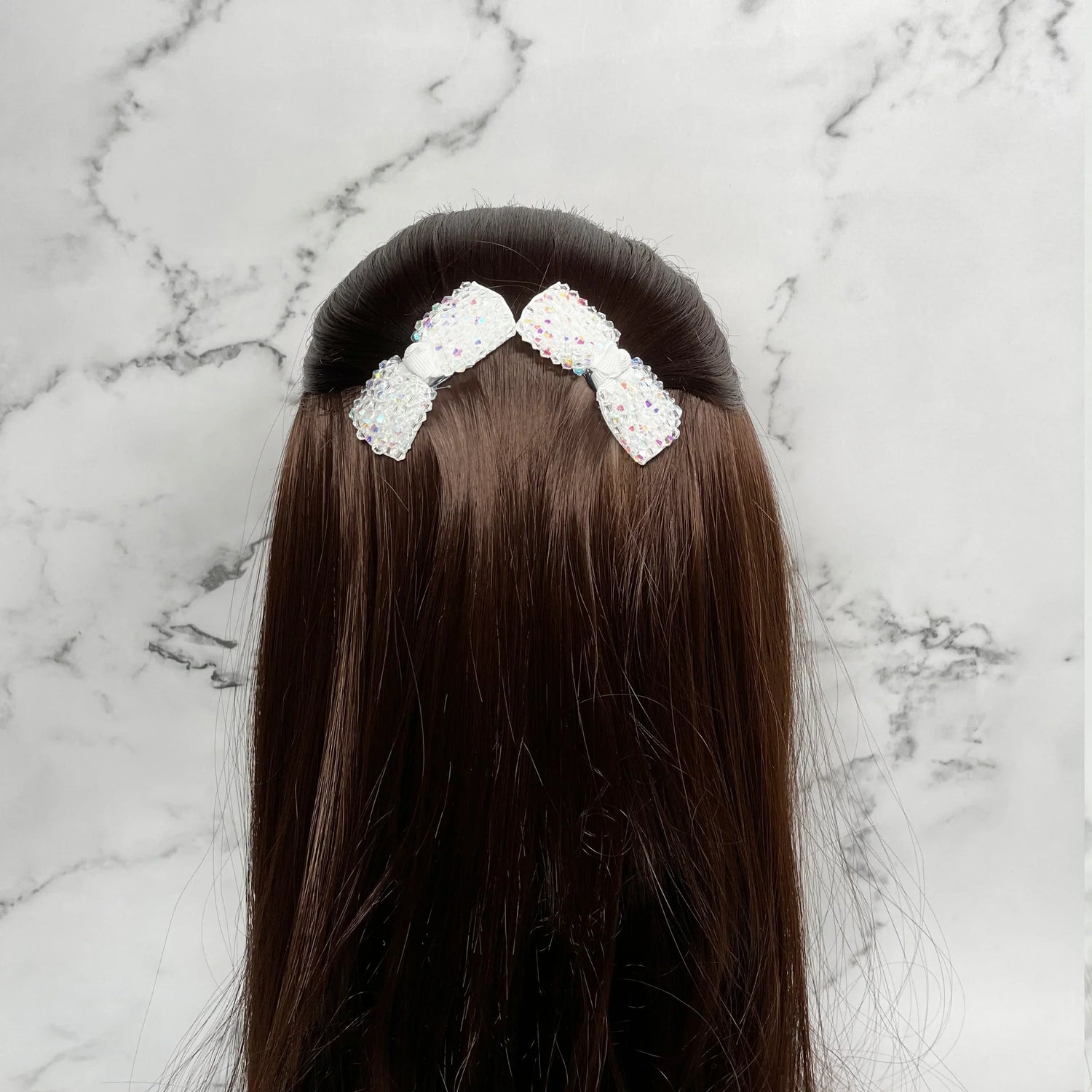Three decorative white bow hair pins placed on dark brown hair against a marble background