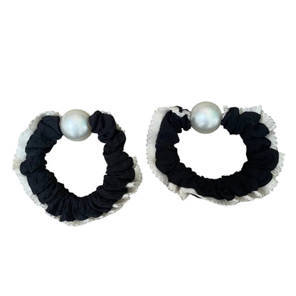 Two black scrunchies with white pearls on a beige background