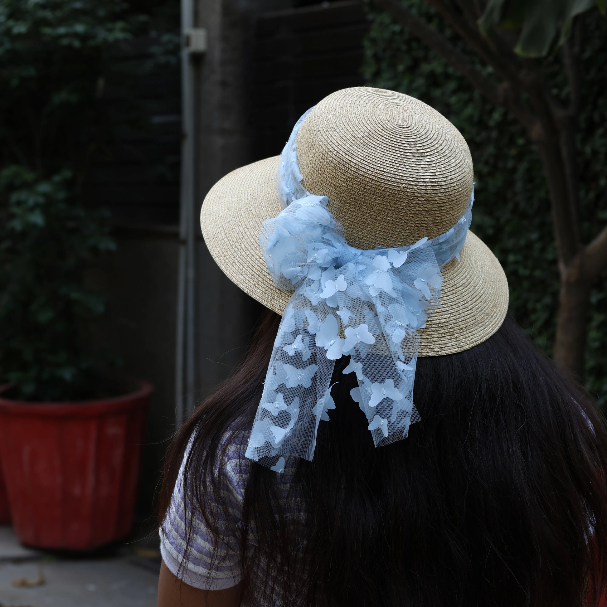Beige straw round hat with blue ribbon worn by woman with long dark hair outdoors