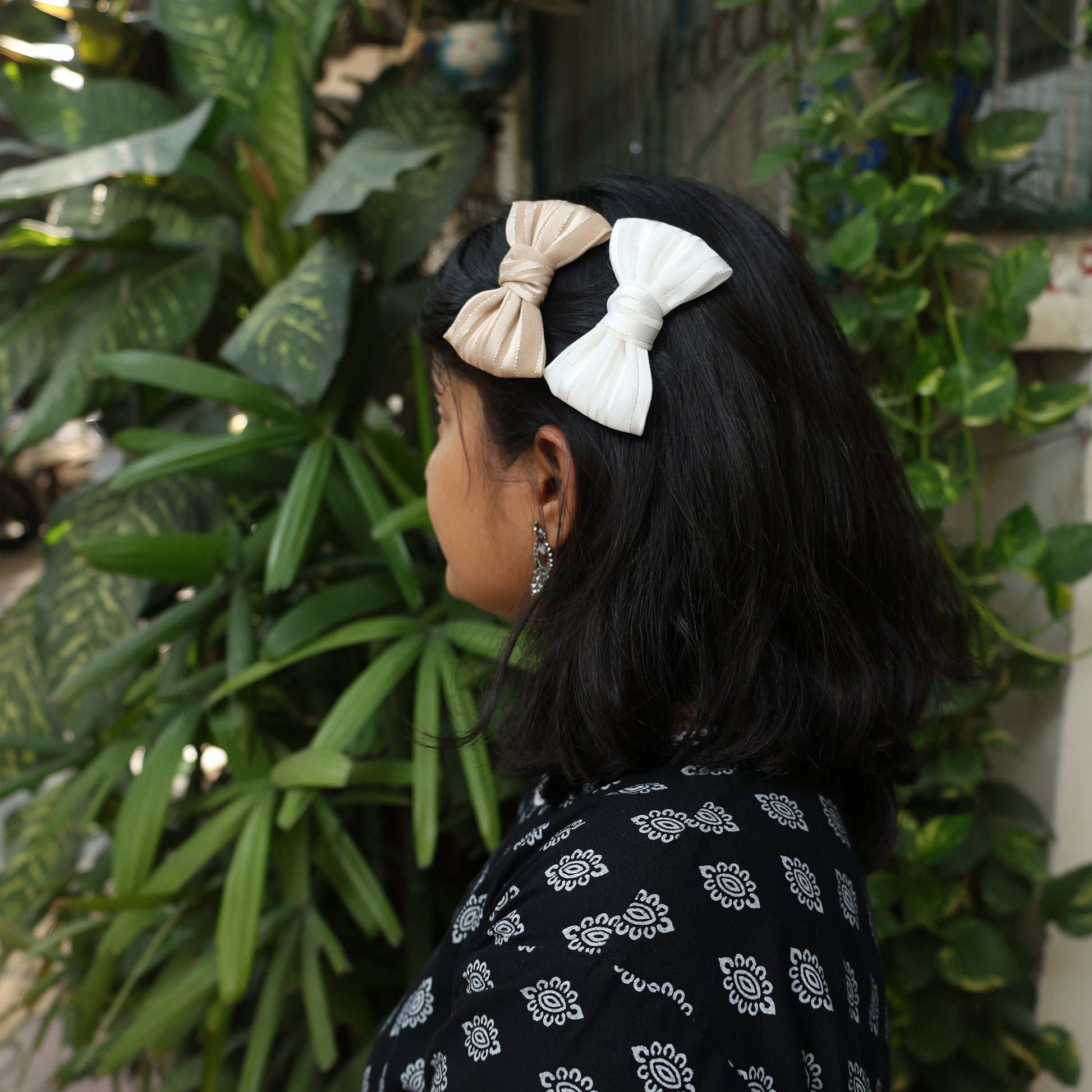 Bella Luxe soft georgette bow clips in beige and white worn on dark hair with green plant background