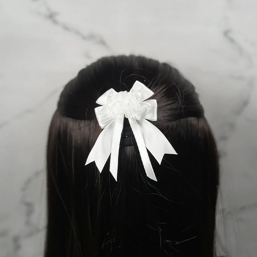 White satin bow clips for kids attached to dark brown hair against a marble background