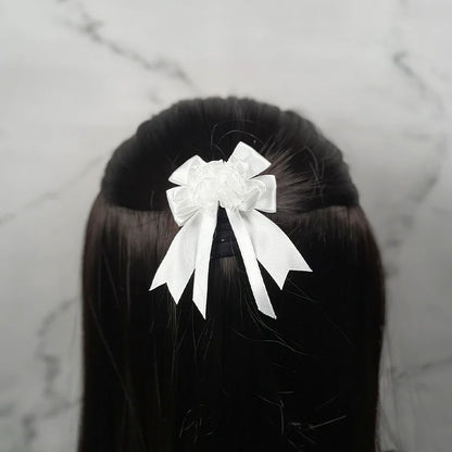 White satin bow clips for kids attached to dark brown hair against a marble background
