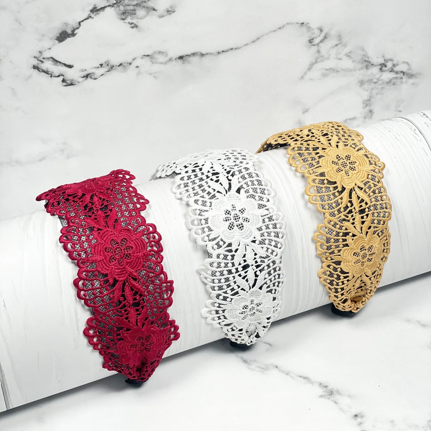 Broad lace hairbands in red white and beige floral design displayed on white surface
