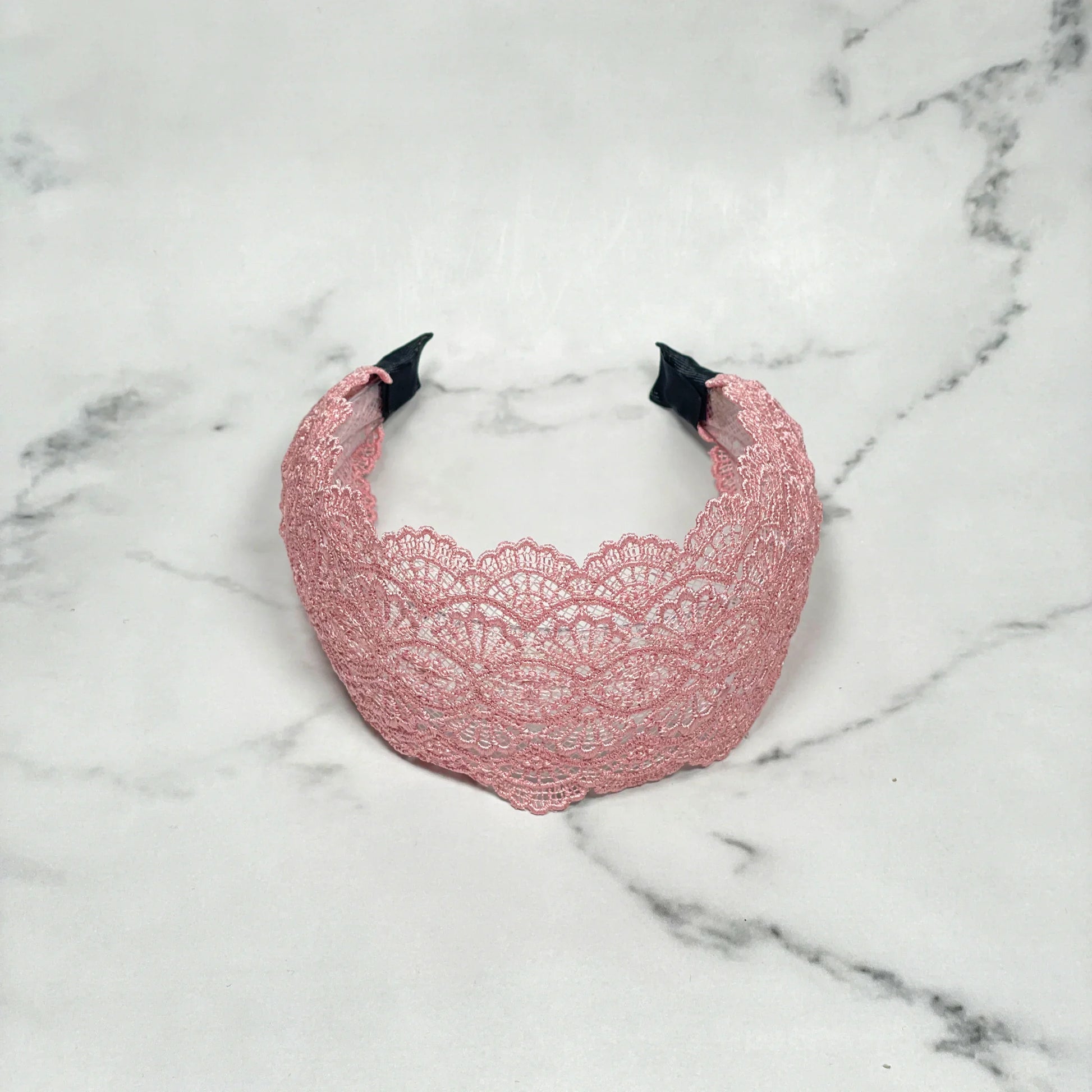 Pink broad lacy hairband with intricate floral lace pattern on a marble surface