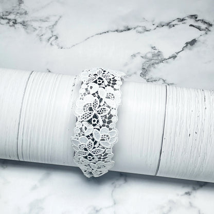 White broad lacy hairbands with floral lace design displayed on white textured surface