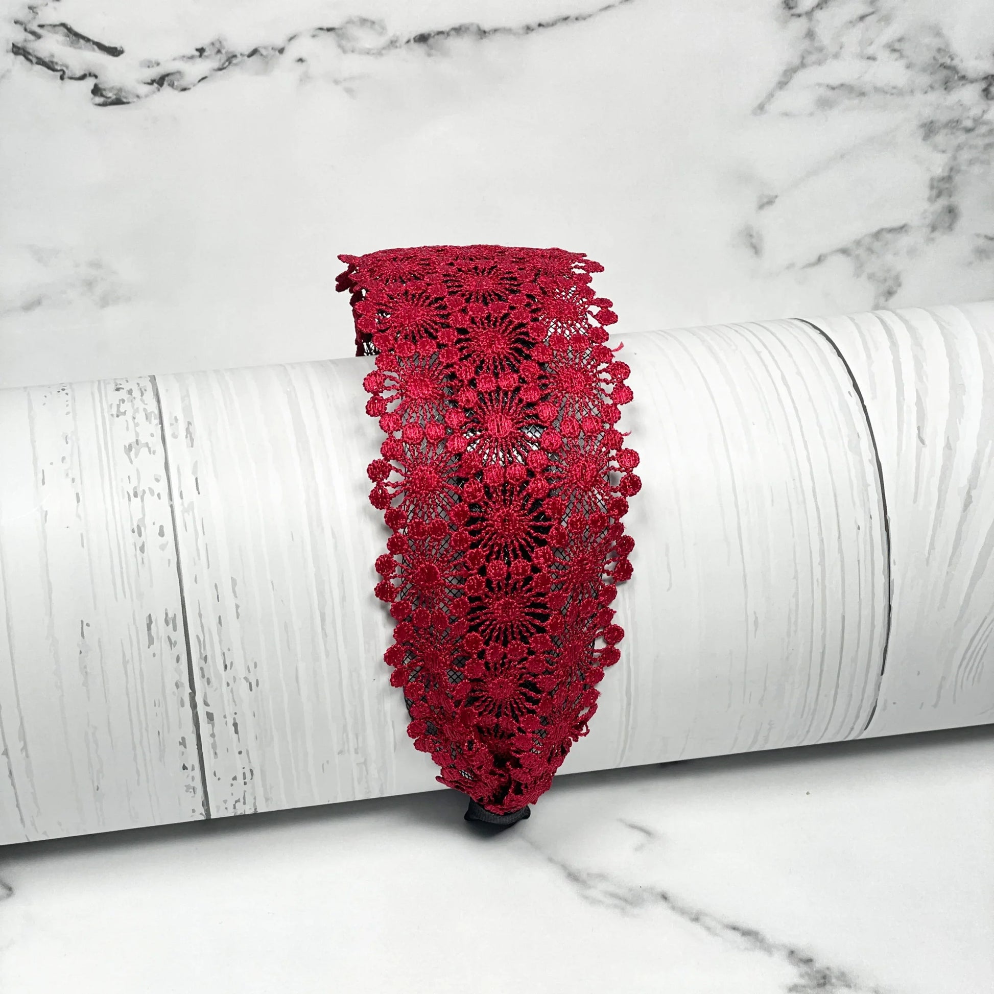 Broad red lacy hairband with intricate floral lace design displayed on white textured background