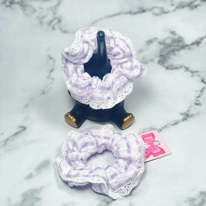 Purple check scrunchies with lace displayed on black holder and marble surface