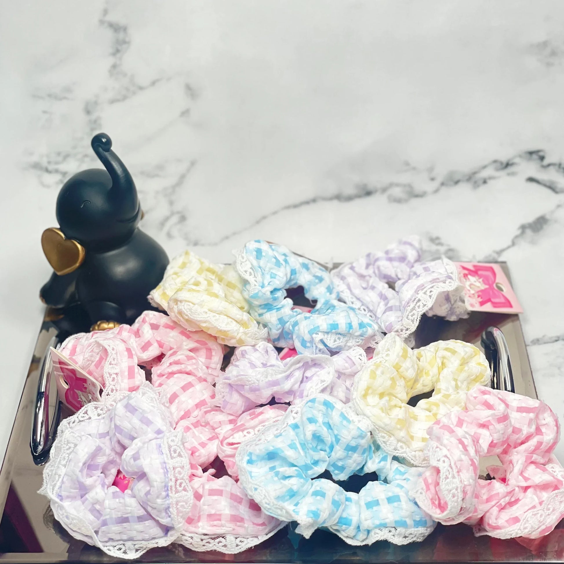 Colorful check scrunchies with lace trim displayed on a reflective tray with a black elephant figurine