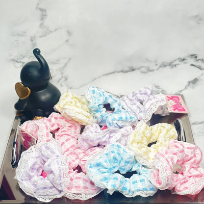 Colorful check scrunchies with lace trim displayed on a reflective tray with a black elephant figurine