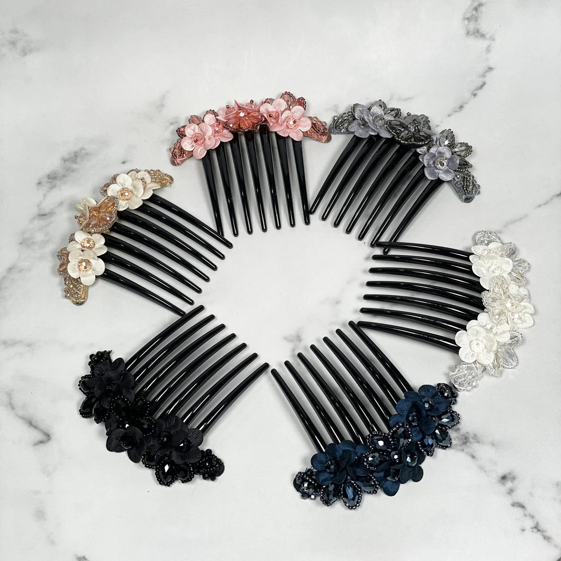 Set of colorful crystal studded comb clips with floral designs arranged in a circle on marble surface