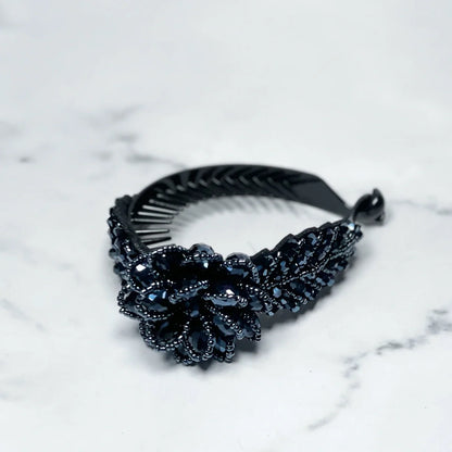 Black crystal studded hair bun clip with floral design on marble surface