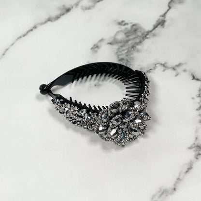 Black plastic crystal studded hair bun clip with intricate floral design on a marble surface