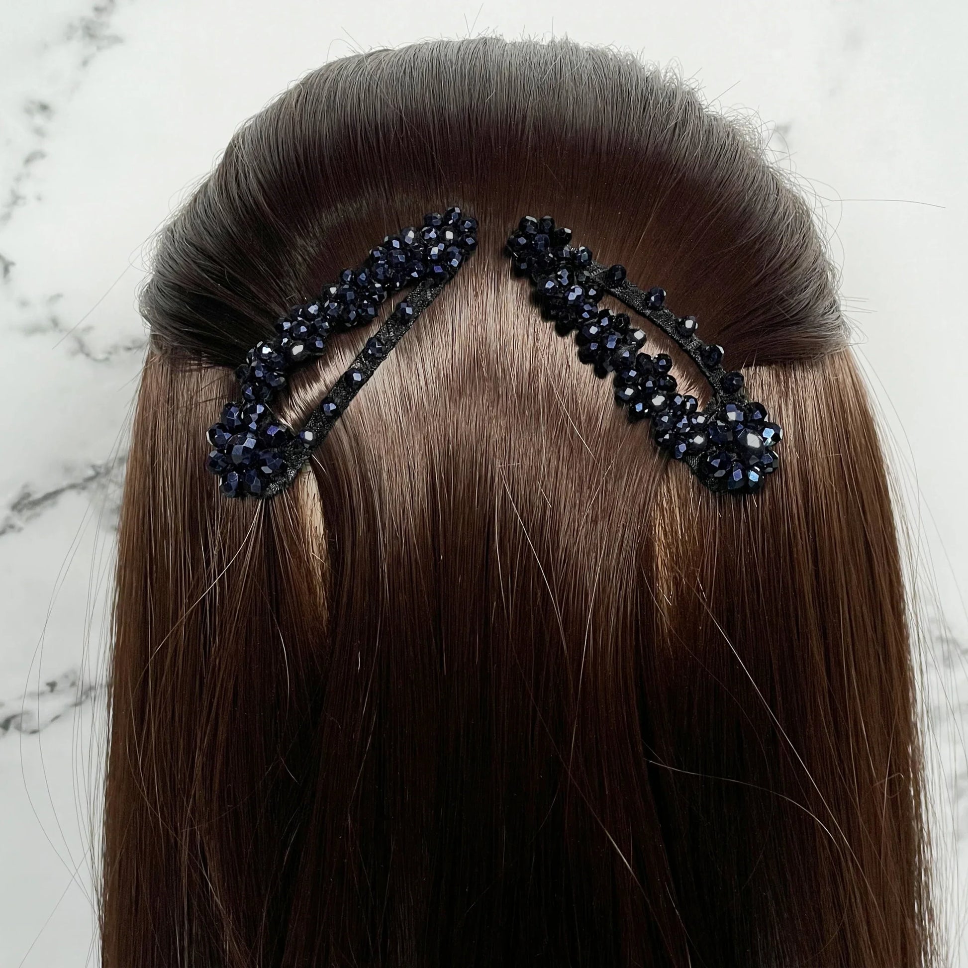 Black crystal studded hair pins worn on brown hair with a marble background