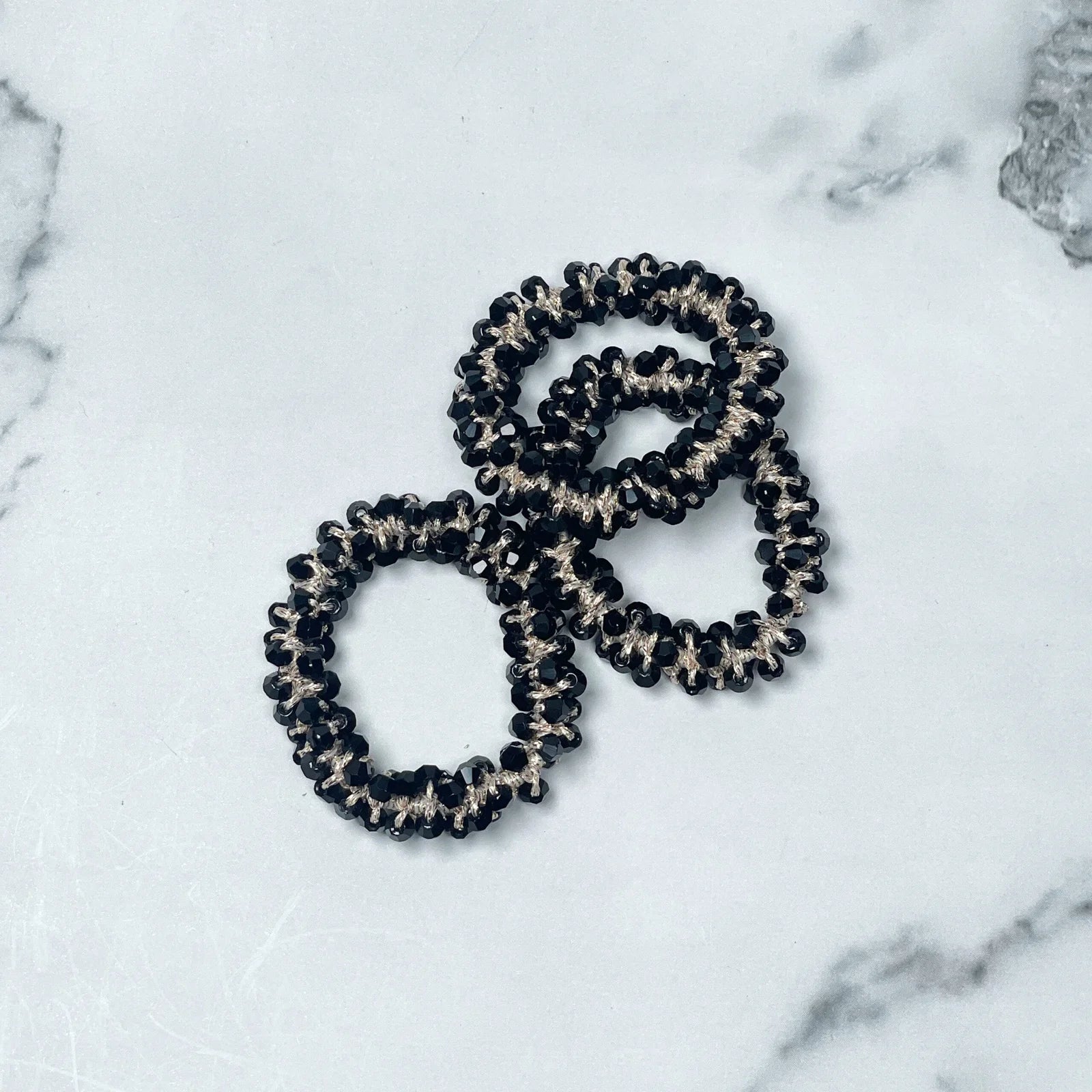 Black and silver crystal studded hair ties arranged on a white marble surface