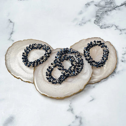 Black crystal studded hair ties displayed on white marble background with decorative agate coasters