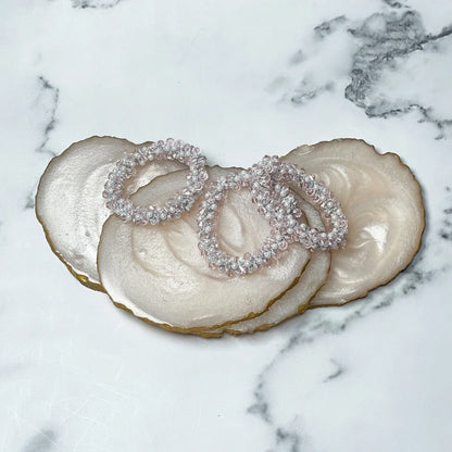 Set of clear crystal studded hair ties displayed on pearlescent stone coasters